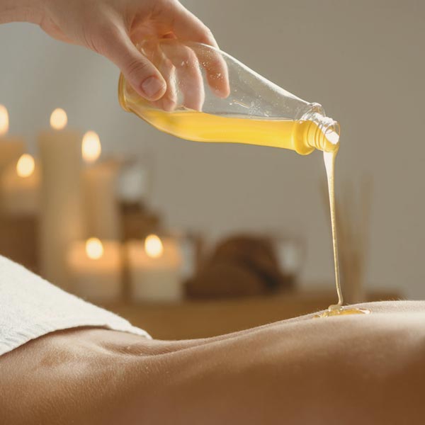 massage practitioner pouring plant-based aroma oil on patient's back